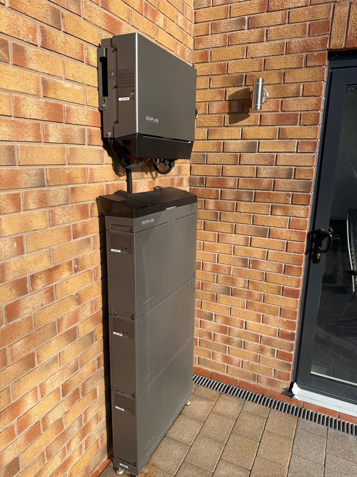Stacked EcoFlow modular battery cells neatly installed alongside the inverter on an external brick wall