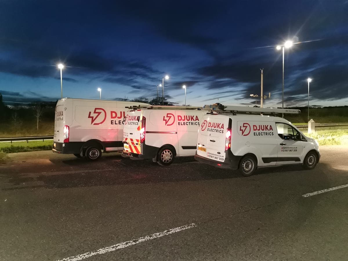 Three Djuka Electrics vans parked at twilight under street lights